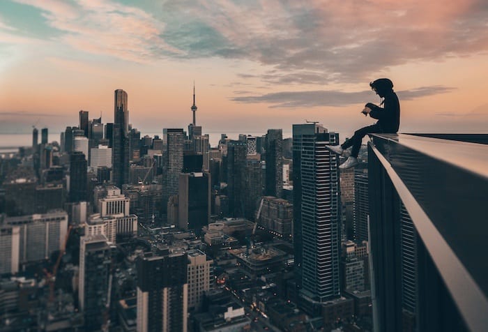 Person sitting on the edge of a building overlooking city.